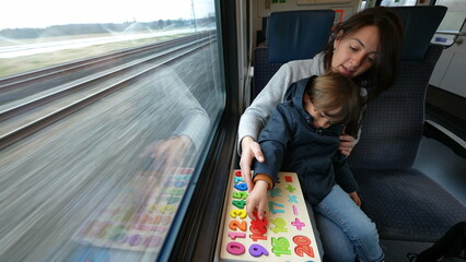 Attentive mom and son delving into an educational exercise while on a rapid train journey, making...