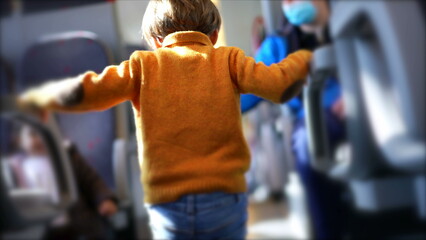 Back of Child clutching into train arm rest playing by himself while on commute, little boy passing the time while traveling on modern transportation wearing yellow pullover and boots