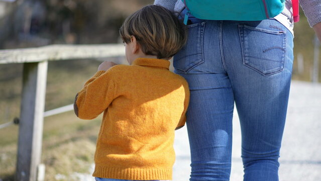 Back of child holding hands with mom walks in outdoor pathway forward