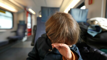Child rubbing eye with hand while traveling by train. Small boy scratching face taking care of itch