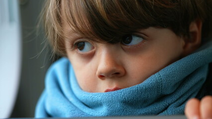 Close-up of a contemplative young caucasian boy, ensconced in a scarf, reflecting a depth of...