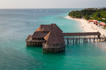 Panorama of coastline at sunny day, drone view of sandy beach, turquoise ocean, luxury resort and beautiful thatch stilt house restaurant, Zanzibar,Tanzania
