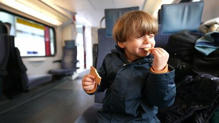 Child snacking butter biscuit seated in train transportation. One caucasian small boy enjoying...