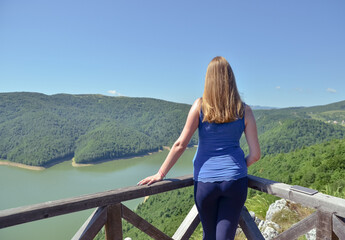 Naklejka premium Rear view at happy free woman enjoying beautiful view of mountains and lake