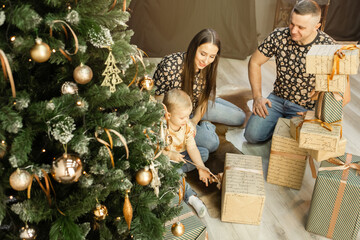 a young family with a small child unwraps gifts near the Christmas tree. family in the living room...