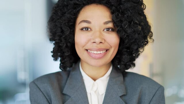 Portrait of a young happy african american businesswoman in a suit standing at workplace in business office. Smiling black woman is posing looking at camera. Headshot of a successful manager. Close up