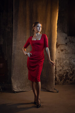 A femme fatale in a red dress. Attractive blonde in an elegant dress with a neckline, sexy and feminine image. photo in dark colors on a textured wall, warm light