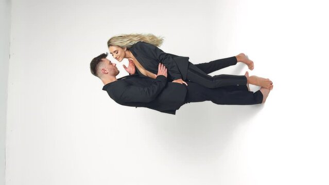 Caucasian young couple wearing black suits stand in studio. Couple stroking each other. White backdrop. Vertical screen.