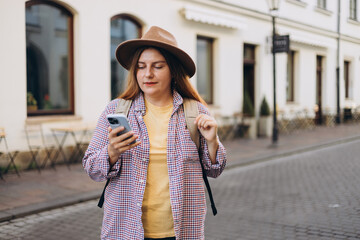Picture of pretty young woman staying on the street holding phone in hands. 30s tourist walking on old city street checks her smartphone. Use technology concept, Traveling Europe in spring
