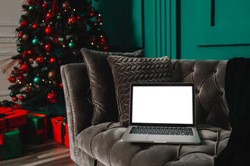 Laptop with blank screen on a desktop and Christmas tree with lights in the background