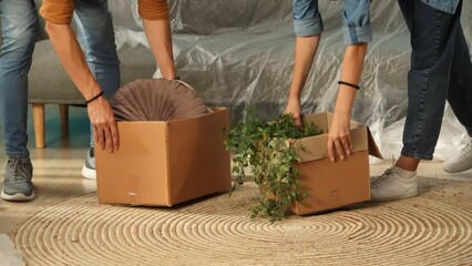 Close up shot of apartment living room. Man and woman hands putting boxes with stuff and plants in...