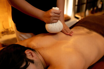 Hot herbal ball spa massage body treatment, masseur gently compresses herb bag on man body....