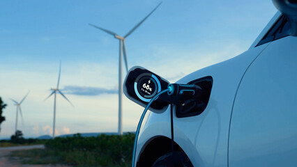 Electric car recharging energy from EV charging station display futuristic smart battery status hologram by EV charger plug cable in wind turbine farm. Alternative clean energy sustainability. Peruse