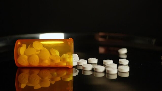 Prescription pill bottle falling at the table and scatter medications in slow motion. Opioid crisis in America, narcotic addiction and overdoses by substance abuse.