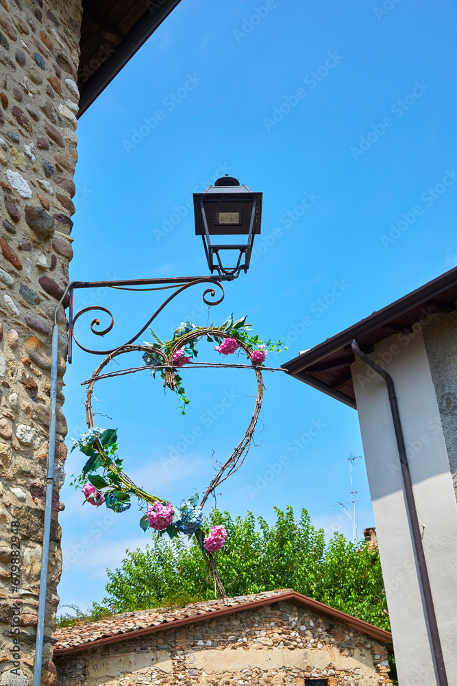 Wall mural Beautiful view of the alleys of the historic old town centre in Castellaro Lagusello, Monzambano, Lombardy, Italy. With street lamps decorated with hearts.