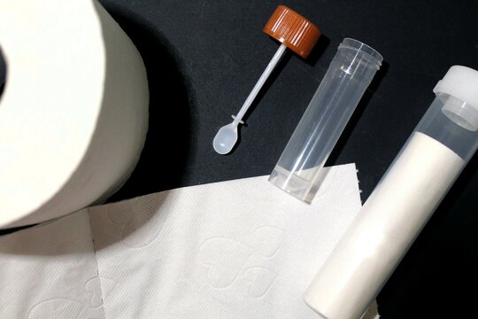 Stuhlprobe: Röhrchen und kleiner Löffel für eine ärztliche Untersuchung des Stuhls. Toilettenpapier. Eine wichtige Untersuchung zur Vorbeugung von Darmkrebs.
