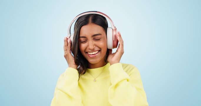 Singing, dance or Indian woman listening to music, podcast or radio audio on subscription in studio. Eyes closed, headphones or happy girl streaming a song isolated on a blue background for wellness