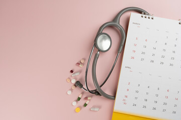 Top view of stethoscope and calendar on the pink background, schedule to check up healthy concept