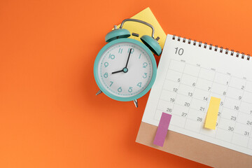 close up of calendar and alarm clock on the orange table background, planning for business meeting or travel planning concept - obrazy, fototapety, plakaty