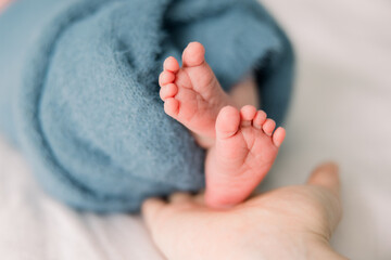 A baby is wrapped up in a blue blanket, his newborn foot and toes are sticking out. - obrazy, fototapety, plakaty