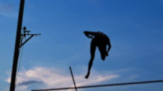 Illustration of the silhouette a female pole-vaulter jumping and failing by dropping the bar.
Blurred background of pro outdoor pole vault and athletics competition. Blurry defocused video footage