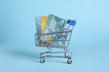 Small metal shopping cart with credit cards on light blue background