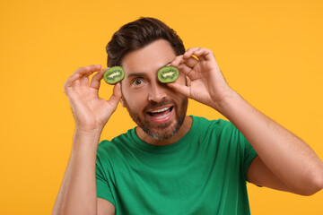 Emotional man holding halves of kiwi on orange background