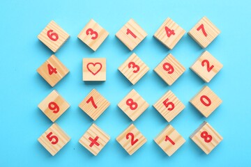 Wooden cubes with numbers and different symbols on light blue background, flat lay