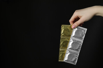 Woman holding condoms on black background, closeup. Space for text