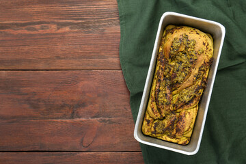 Freshly baked pesto bread in loaf pan on wooden table, top view. Space for text