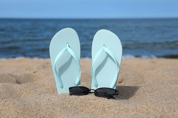 Stylish light blue flip flops and sunglasses on beach sand