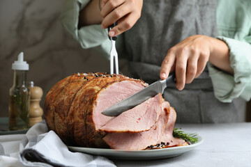 Woman cutting delicious baked ham at light grey table, closeup
