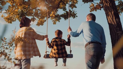 Father and mother united in actions to ride son on homemade swing at sunset