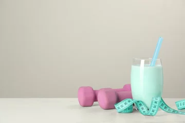 Tuinposter Tasty shake, dumbbells and measuring tape on white table against light gray background, space for text. Weight loss © New Africa