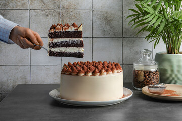 Woman taking piece of delicious tiramisu cake with server at grey table, closeup