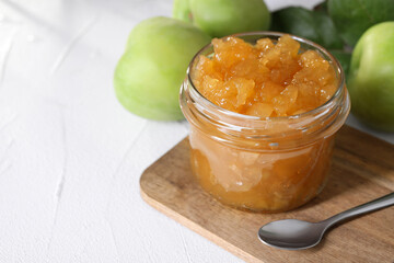 Glass jar of delicious apple jam and fresh fruits on white table, space for text