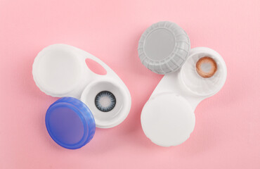 Cases with color contact lenses on pink background, flat lay
