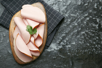 Board with slices of tasty boiled sausage and parsley on dark textured table, top view. Space for text