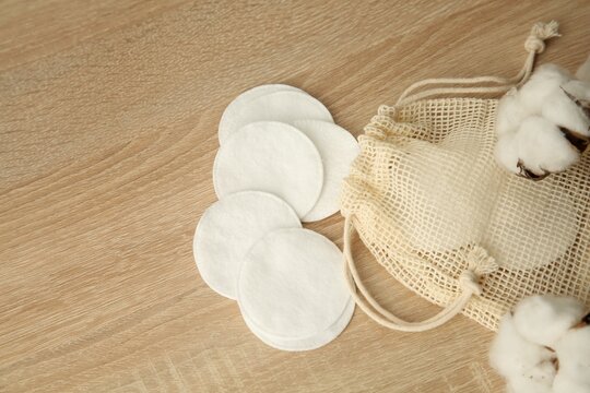 Cotton pads, bag and flowers on wooden table, flat lay. Space for text
