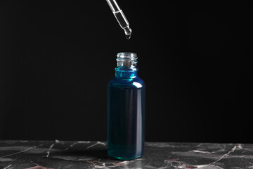 Dripping cosmetic serum from pipette into bottle on grey marble table