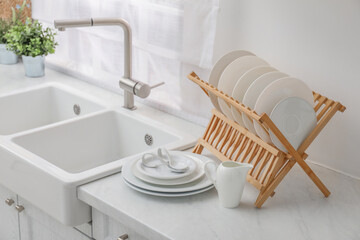 Drying rack with clean dishes on light marble countertop near sink in kitchen