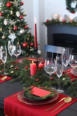 Elegant Christmas table setting with dishware and burning candles in festively decorated room