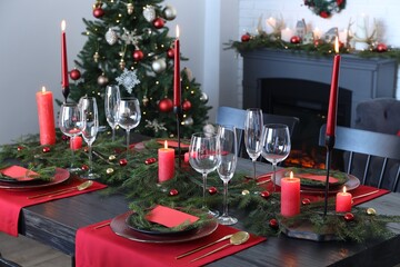 Elegant Christmas table setting with dishware and burning candles in festively decorated room