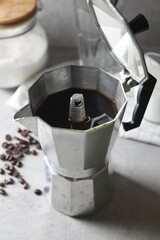 Brewed coffee in moka pot and beans on light grey table