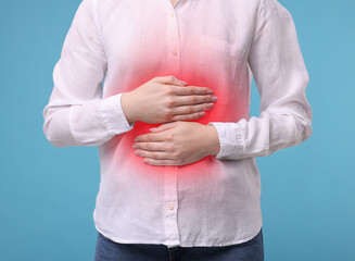 Woman suffering from stomach pain on light blue background, closeup
