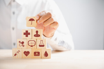 Hand grips wooden block adorned with healthcare and medical icons, symbolizing safety, health, and family well-being. Reflecting pharmacy, heart care, and happiness. health care concept