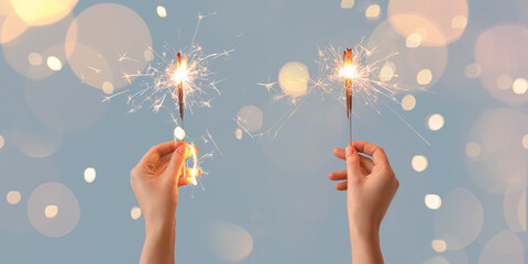 Female hands holding beautiful Christmas sparklers on light blue background
