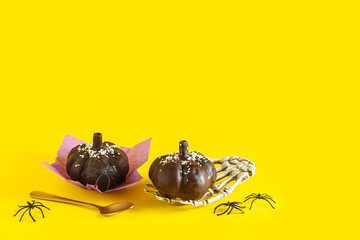 Delicious chocolate cakes, skeleton hand and spoon for Halloween celebration on yellow background