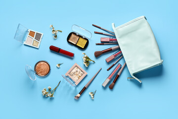 Stylish cosmetic bag with makeup products and beautiful flowers on blue background