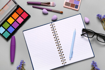 Composition with makeup cosmetics, eyeglasses, beautiful flowers and notebook on grey background